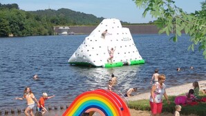 Un parque acuático con un tobogán inflable gigante, una estructura de juego con arcoíris y un lago con barcos al fondo.