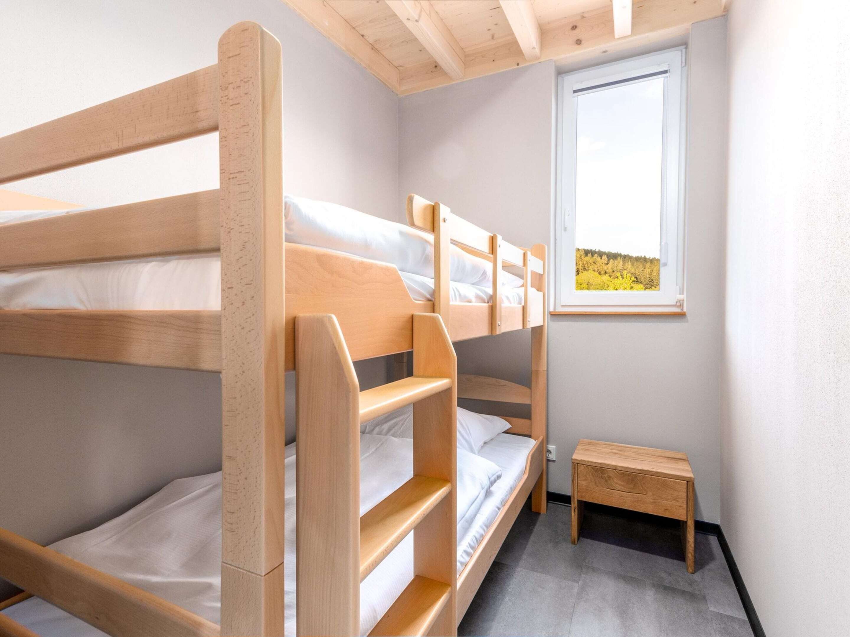 A bunk bed room with a small wooden table and a window with a view of trees.