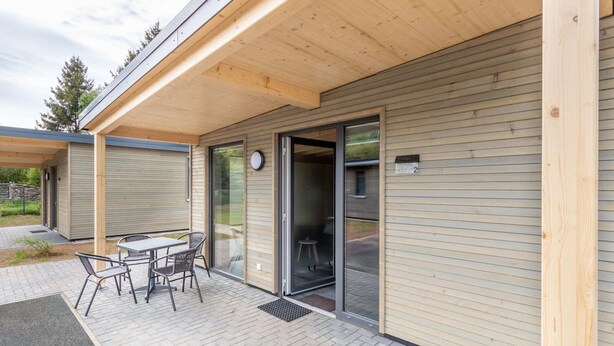 Un edificio moderno con un patio cubierto, puerta de cristal corrediza y una pequeña zona exterior con mesa y sillas.