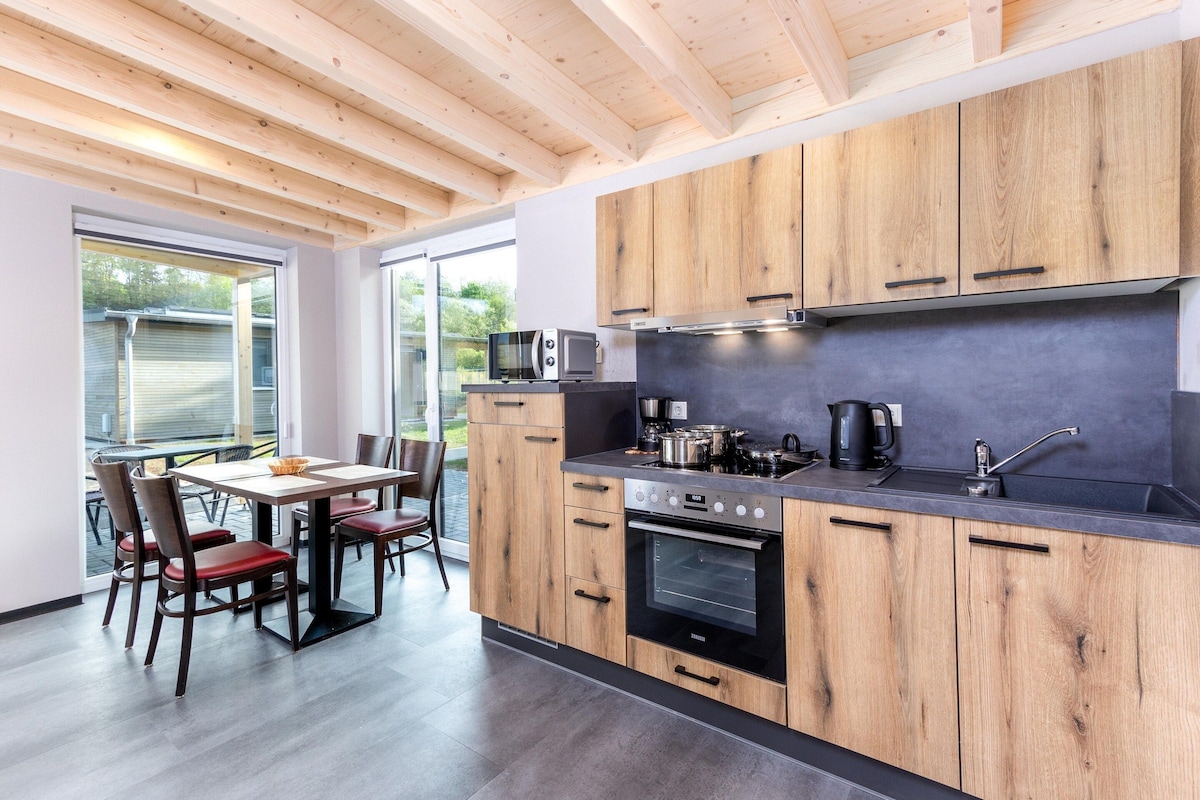 A modern kitchen with wooden cabinets, a built-in oven, and a dining area with a table and chairs.