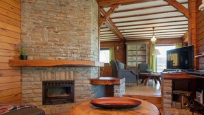 A cozy log cabin interior with a stone fireplace, wooden beams, a television, and a dining table. - Vintage Villa With Private Garden in Rendeux (Rendeux)