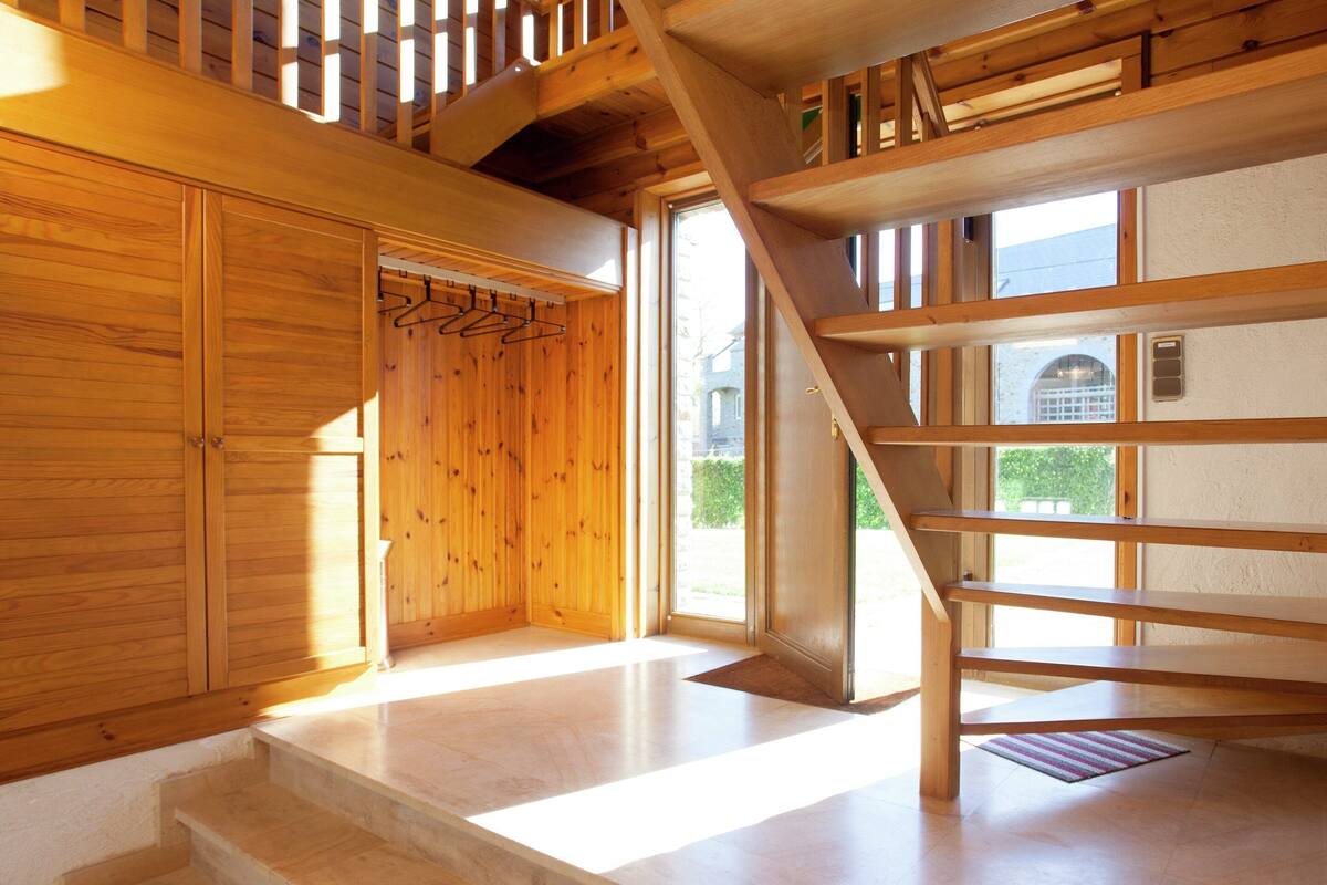 A wooden staircase leading to a second floor, a wooden door with a coat rack, and a view of the outside through a window.