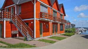 A red building with a staircase leading to a balcony, a satellite dish, and a view of boats in the background. - Ferienwohnung in Plau am See (Plau am See)