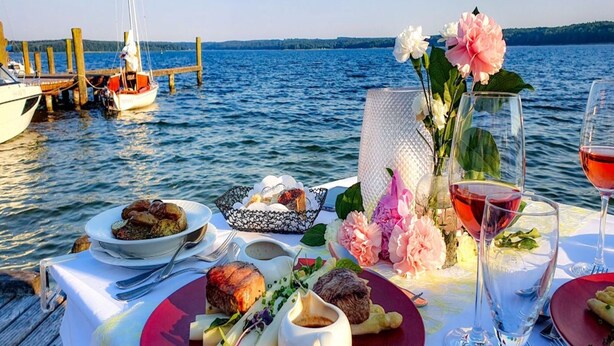 A table set for a meal with food and drinks on a dock by the water. - Ferienwohnung in Plau am See (Plau am See)