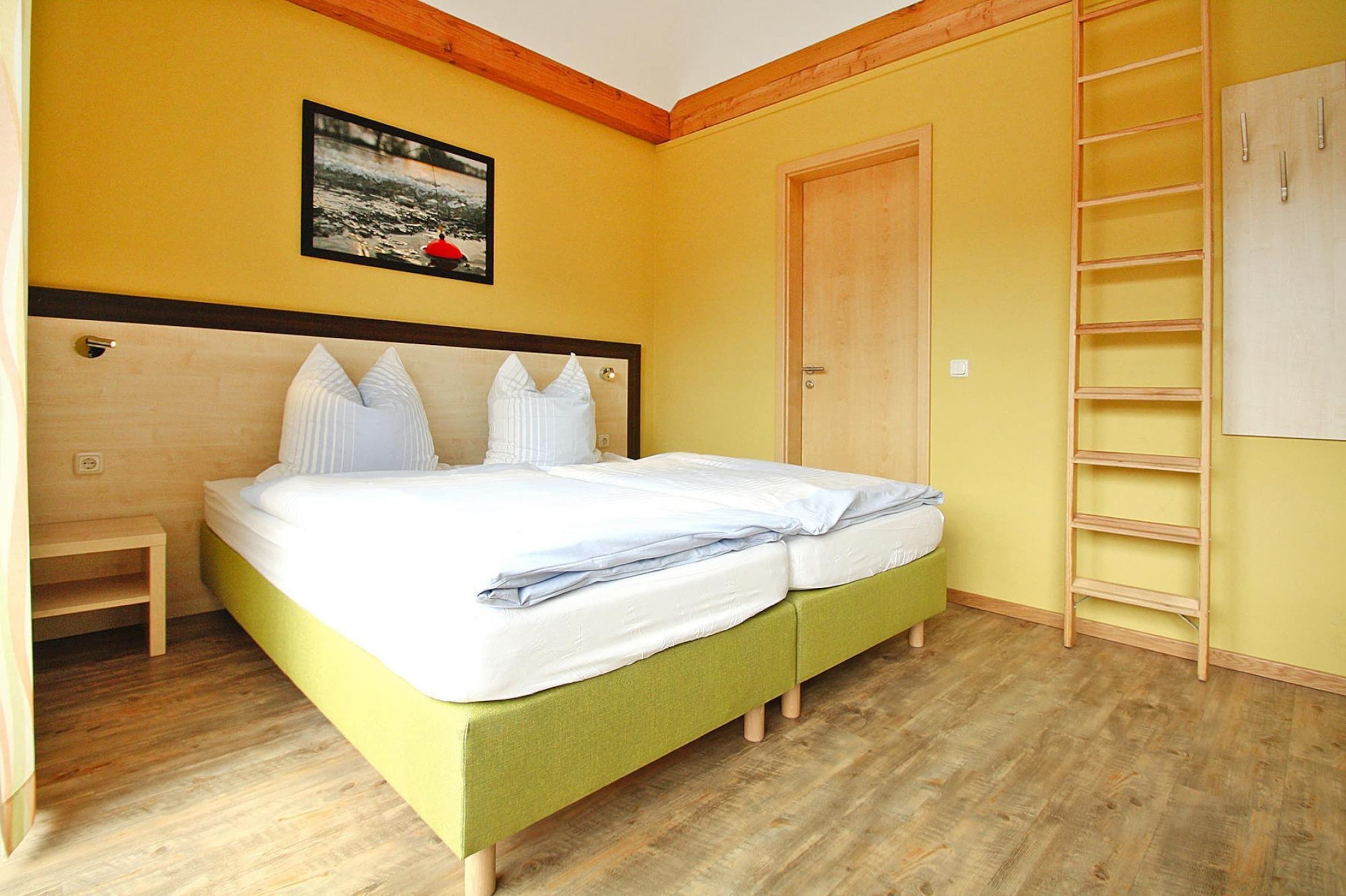 A room with a bed, a wooden ladder, a door, and a picture on the wall.