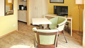 A compact room with a kitchenette, a dining area with a table and chairs, a television, and a framed picture on the wall. - Ferienwohnung in Plau am See (Plau am See)