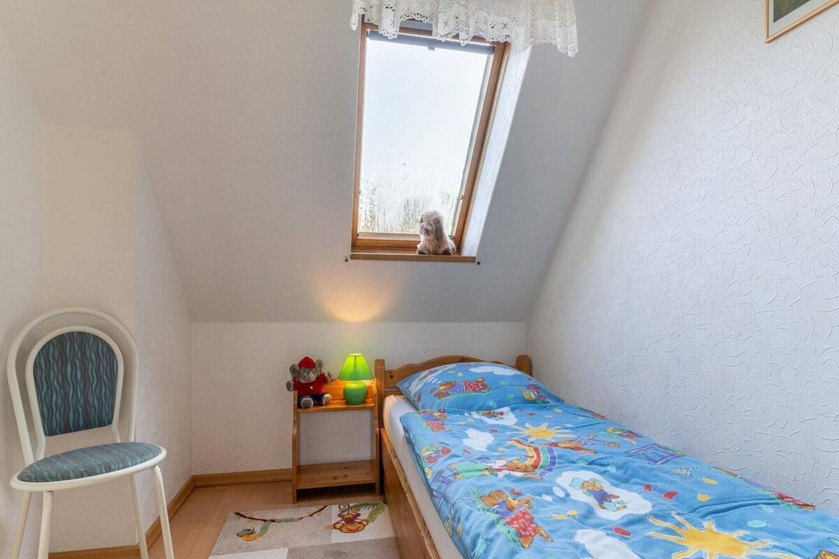 A child's bedroom with a single bed, a chair, a nightstand, a window, and a small table with toys.