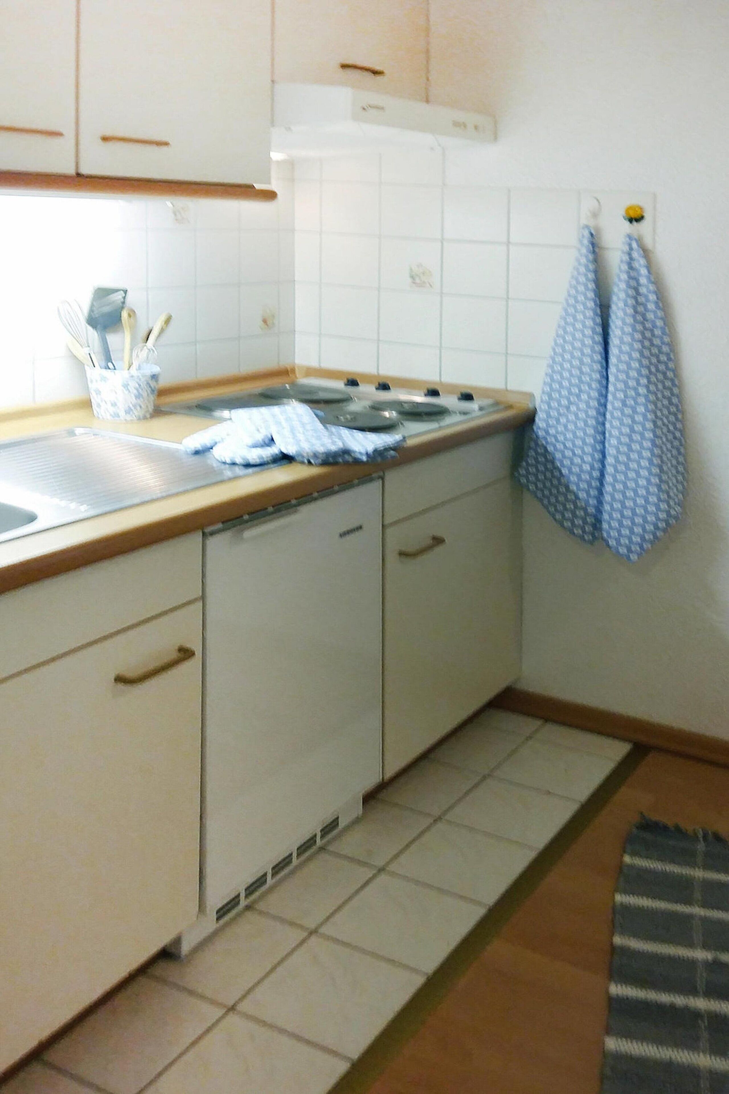 A kitchen with white cabinets, a stove, and a tiled backsplash. There are two blue and white checkered towels hanging on hooks.
