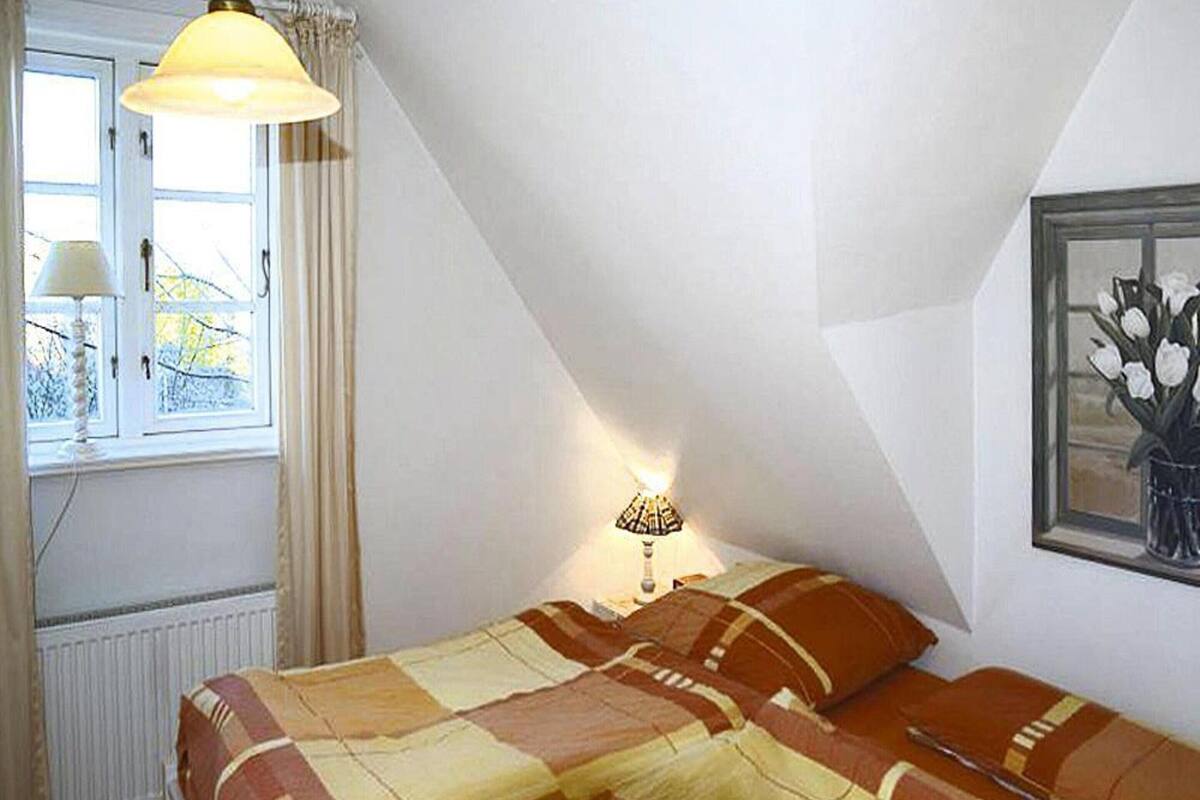 Ein Schlafzimmer mit einem Bett, einem Fenster, einer Heizung, einer Lampe und einem Gemälde.