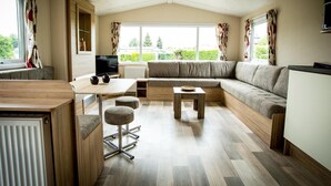 A modern living room with a sectional sofa, a wooden dining table, and a television.
