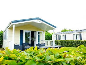 A single-story mobile home with a porch, a small deck, and a garden area in the foreground. - Chalet Near Loonse and Drunense Duinen (Udenhout)