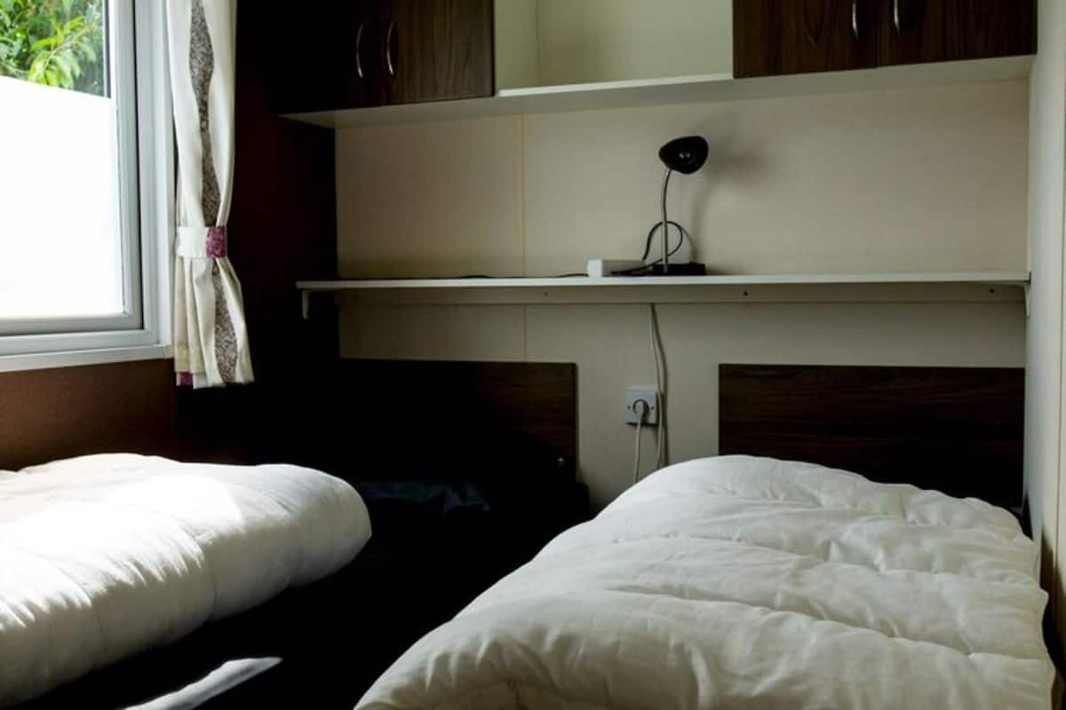 Un dormitorio con dos camas individuales, una mesita de noche, una lámpara y una ventana con cortinas.