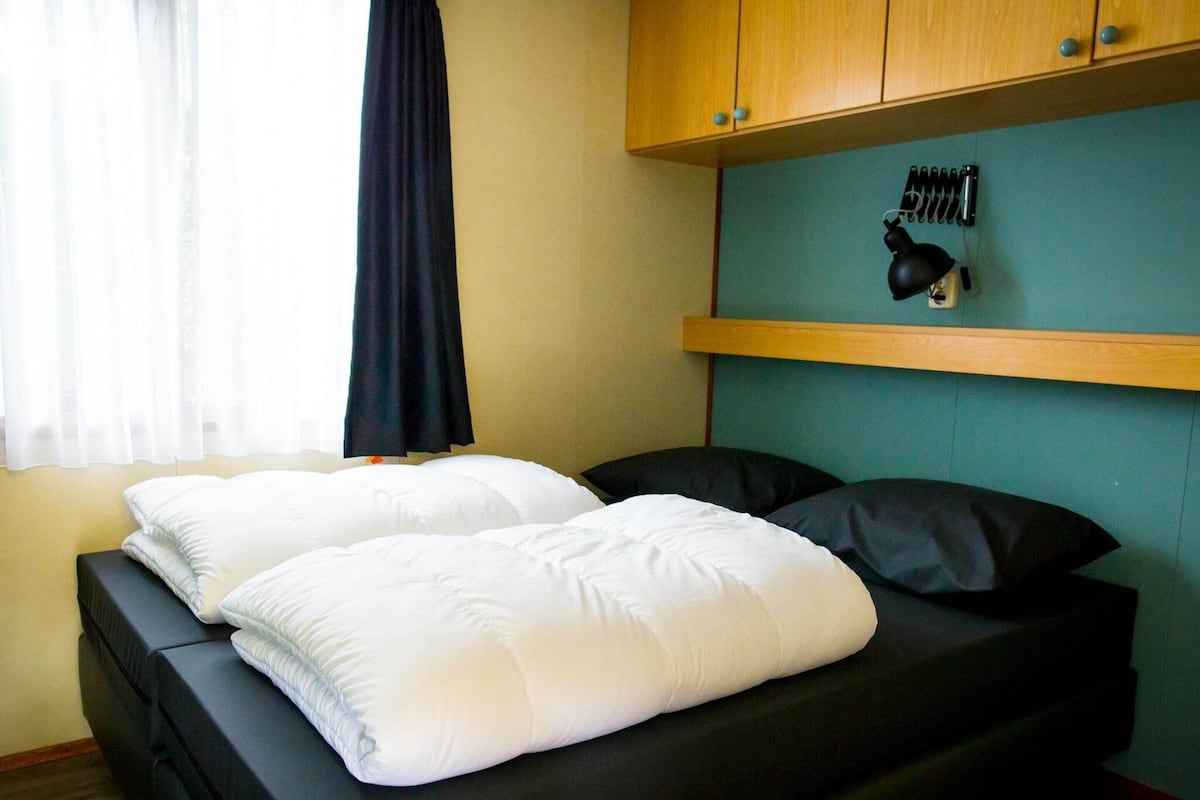 Una cama individual con ropa blanca, cabecera negra y una pared de acento color aguamarina.