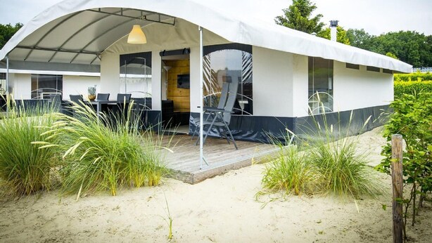 A modern beach house with a covered patio, outdoor seating, and a wooden deck.