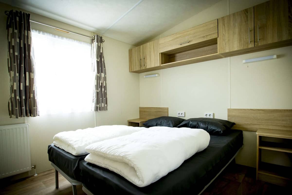 Un dormitorio con cama, cabecera de madera, mesitas de noche y una ventana con cortinas.