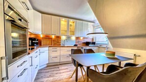 Une cuisine moderne avec des meubles blancs, un plan de travail en bois et un coin repas comprenant une table et des chaises.