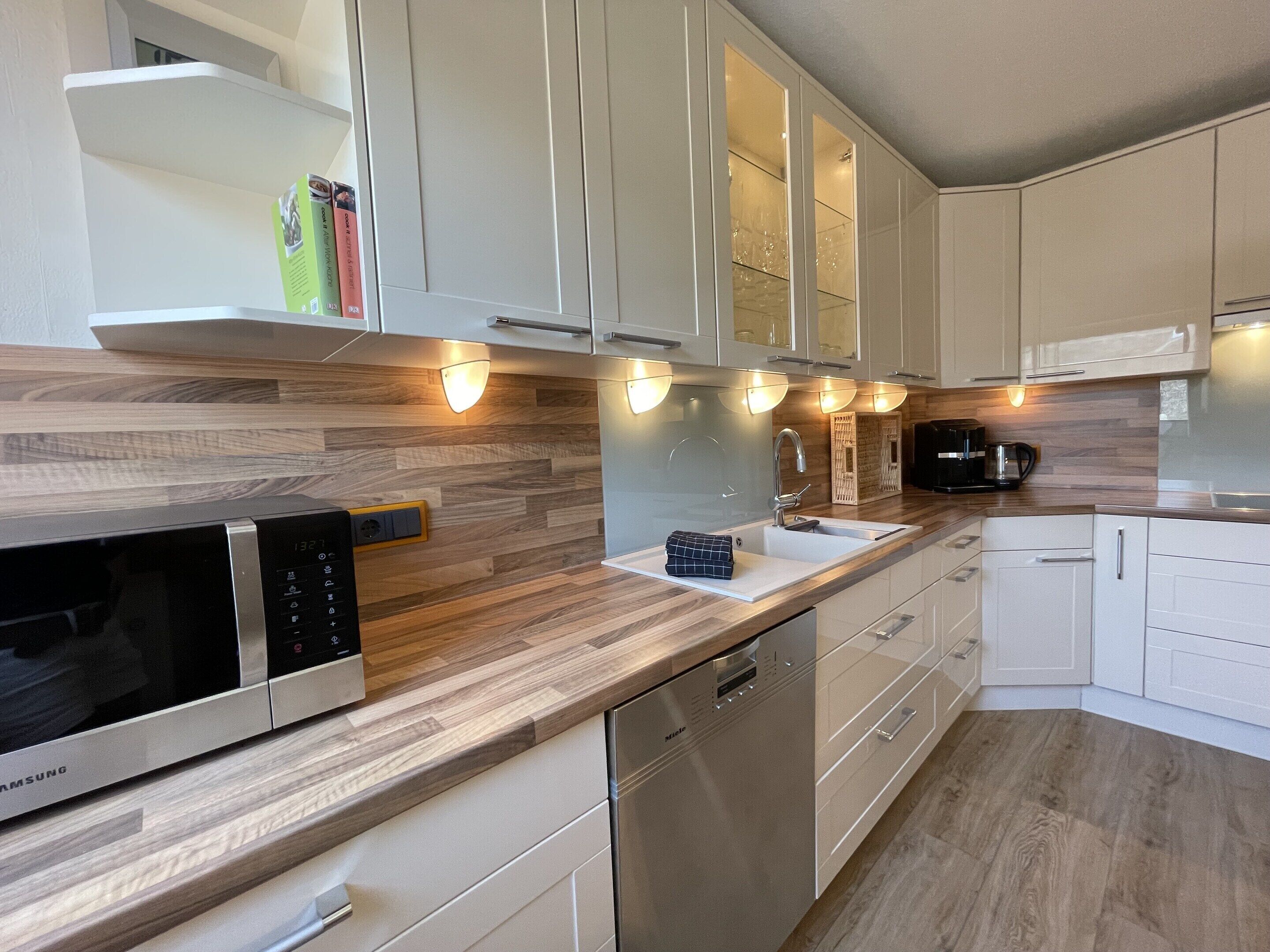 A modern kitchen with white cabinets, a wooden countertop, a built-in microwave, a dishwasher, and a coffee maker.