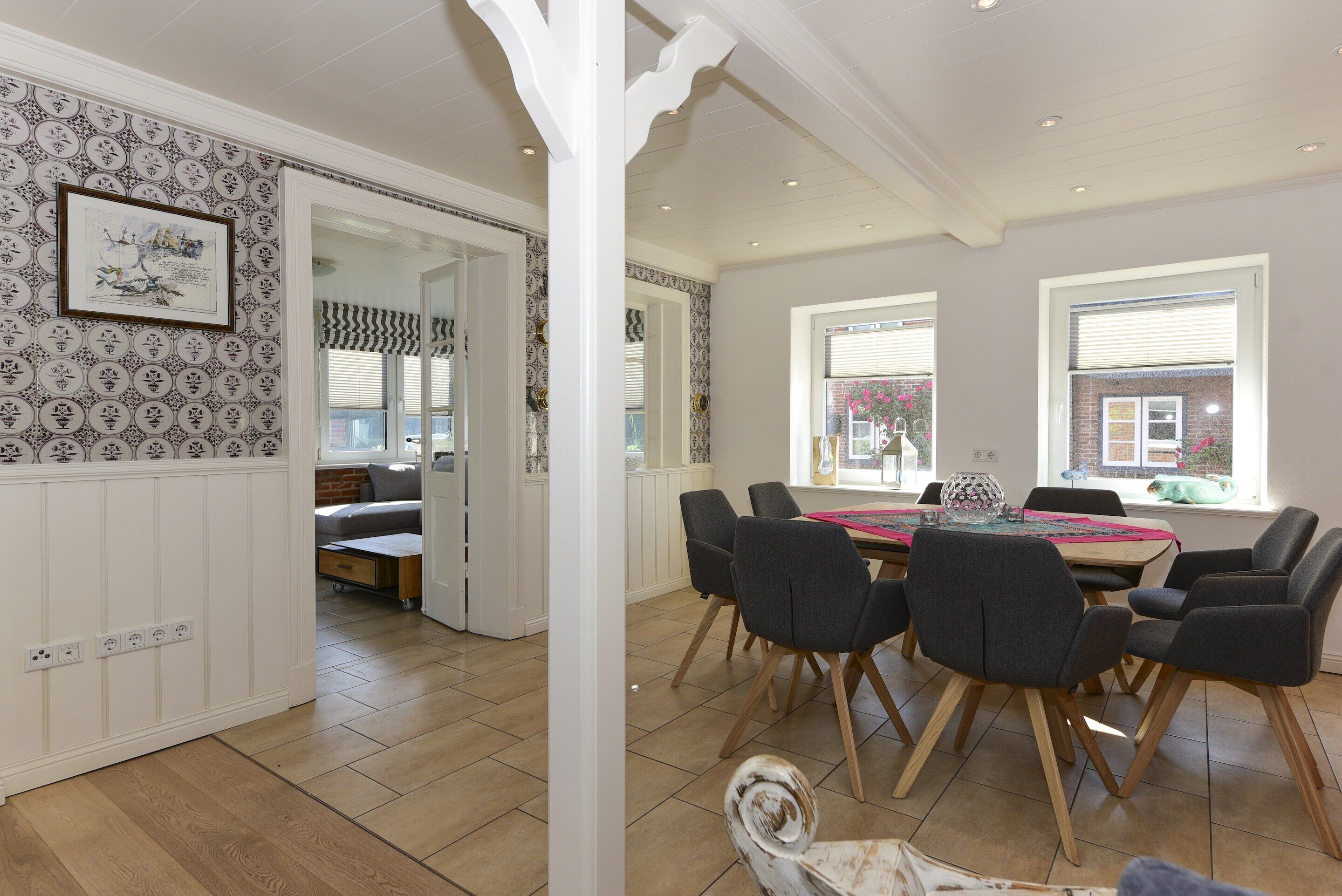 A dining area with a wooden table and chairs, a patterned wallpaper, and a view of the outside through a window.