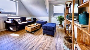 Un salon de style industriel, avec un plafond en pente, un canapé bleu foncé, une table basse en bois et une bibliothèque.