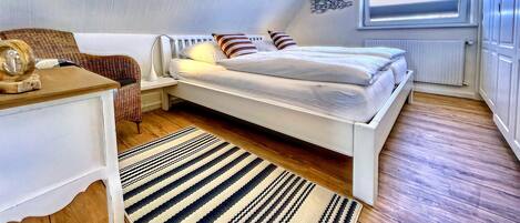A small, well-lit bedroom with a single bed, a nightstand, a chair, and a window.
