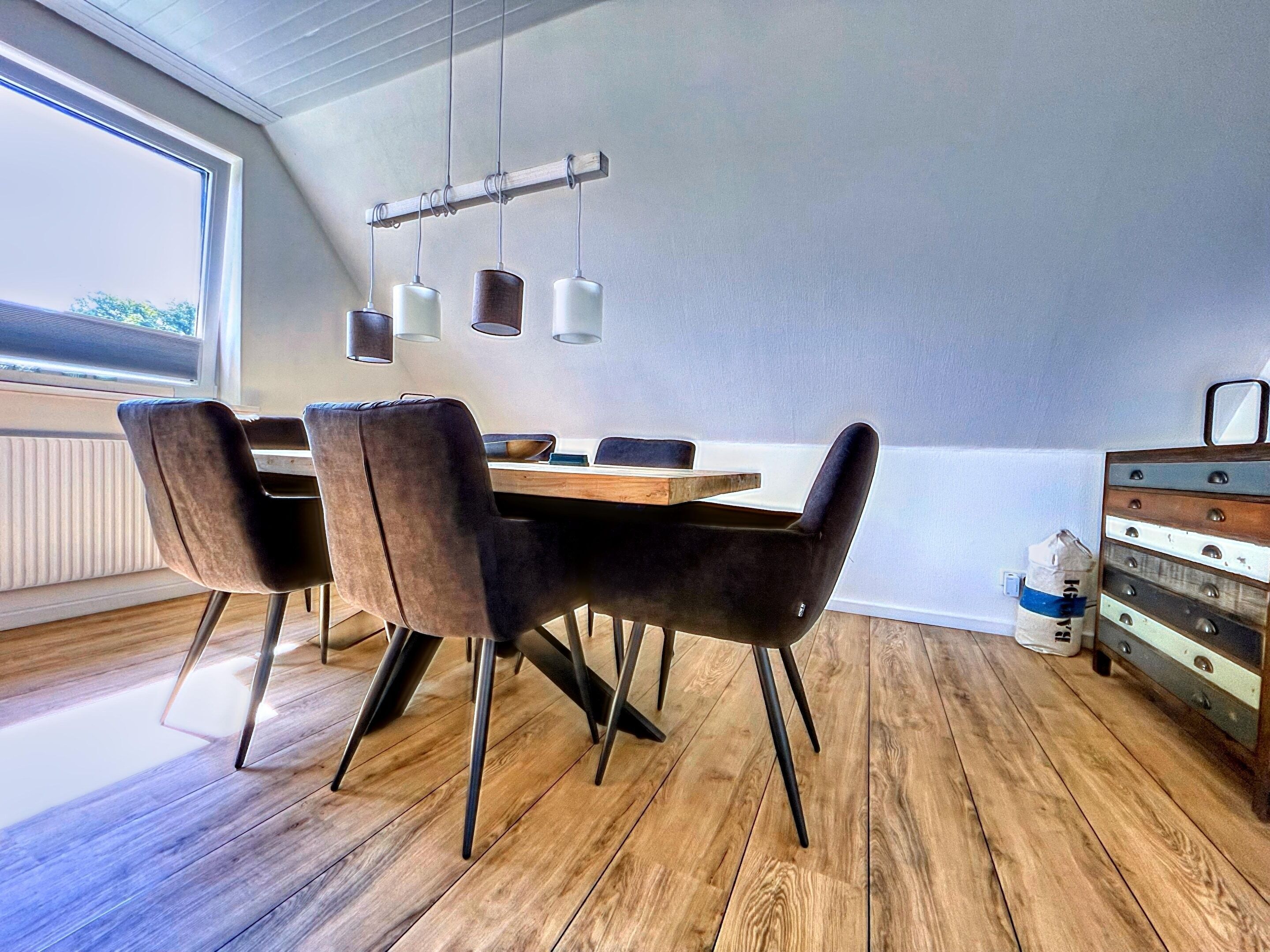 Zona pranzo con tavolo in legno, sedie nere e lampade a sospensione.