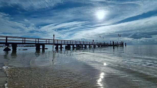 A pier extending into calm water with a clear sky and a bright sun. - Apartments, Wyk auf Foehr (Wyk auf Foehr)