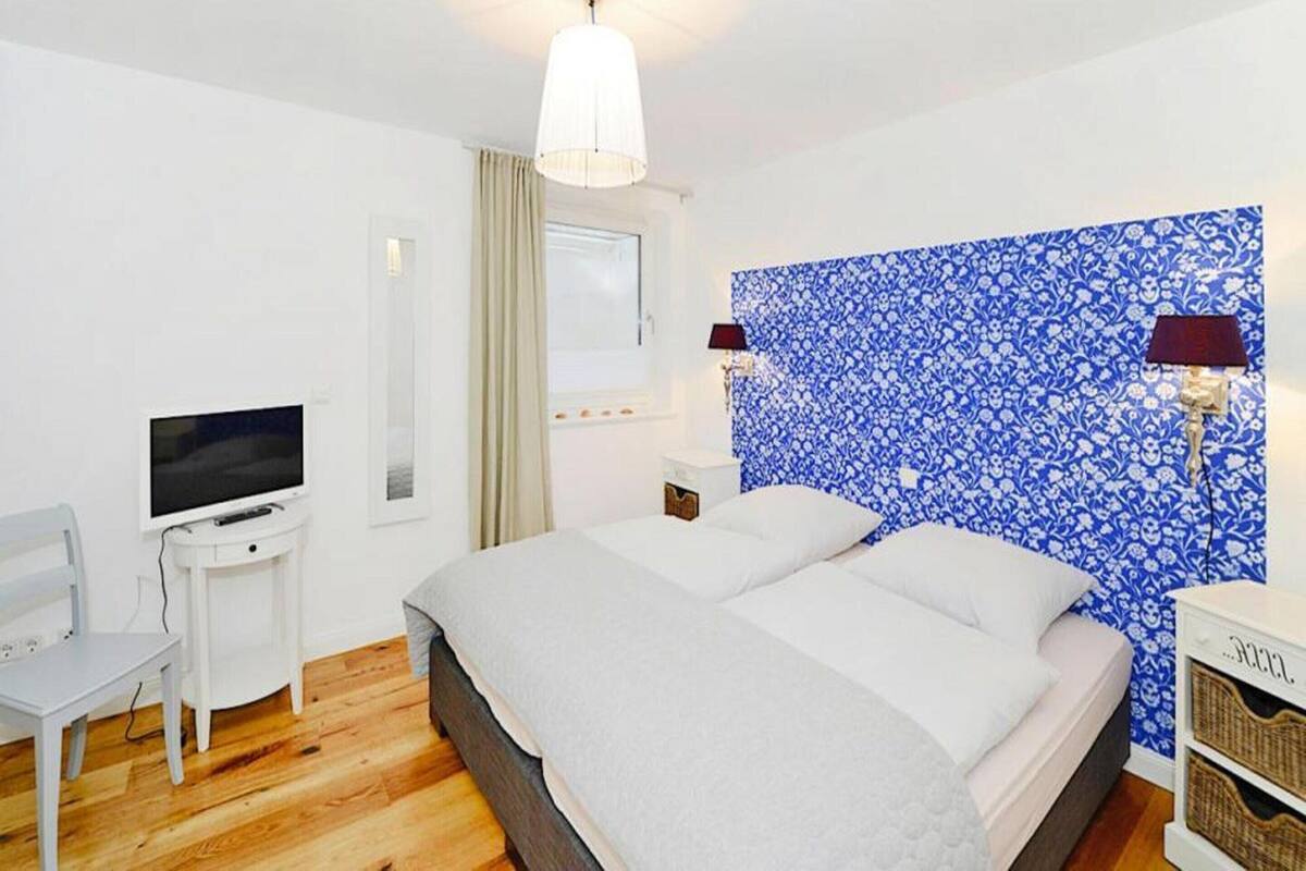 A bedroom with a bed, a TV, a desk, and a window with curtains.