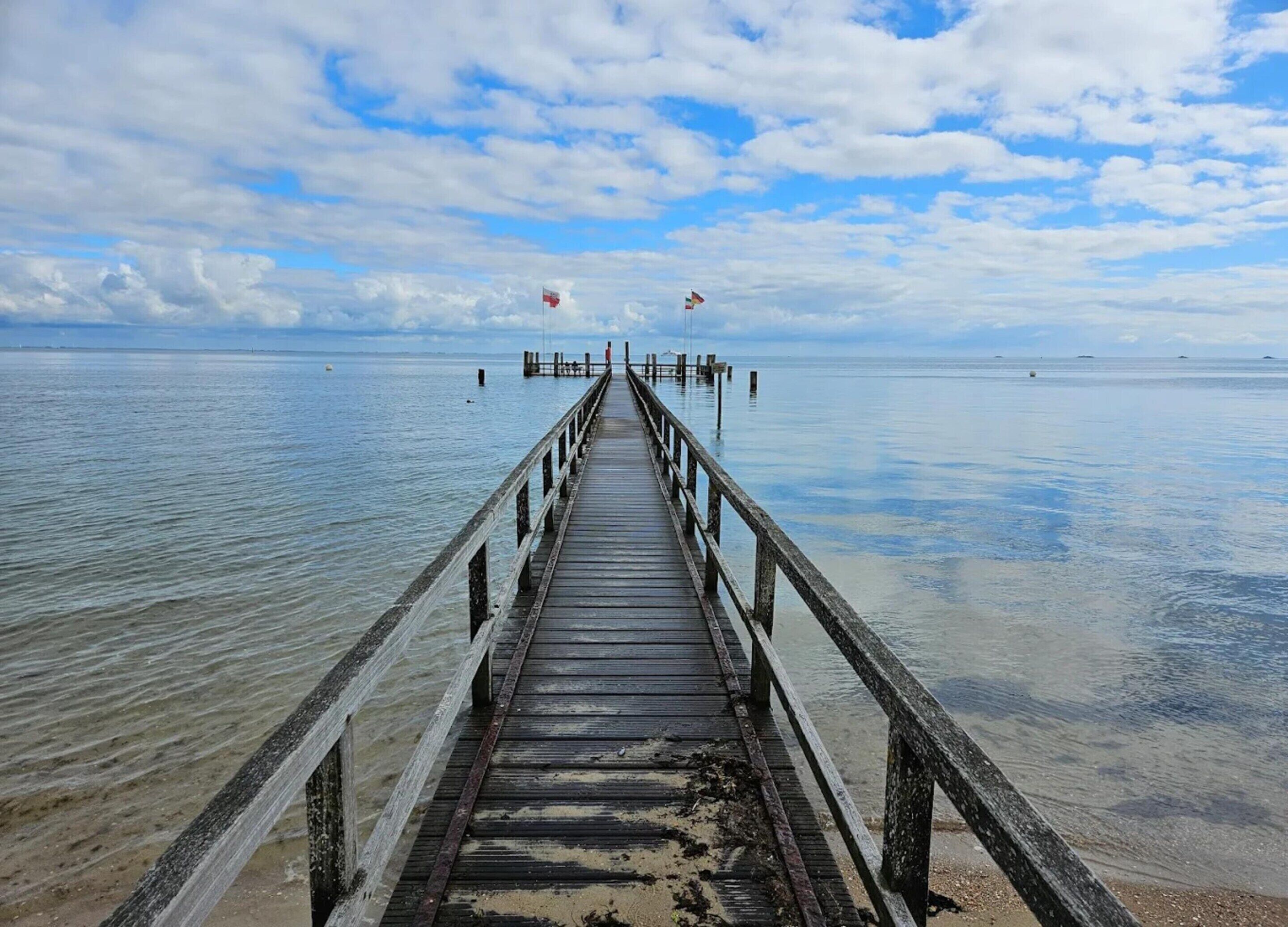 A wooden pier extending into calm waters with a clear sky above.