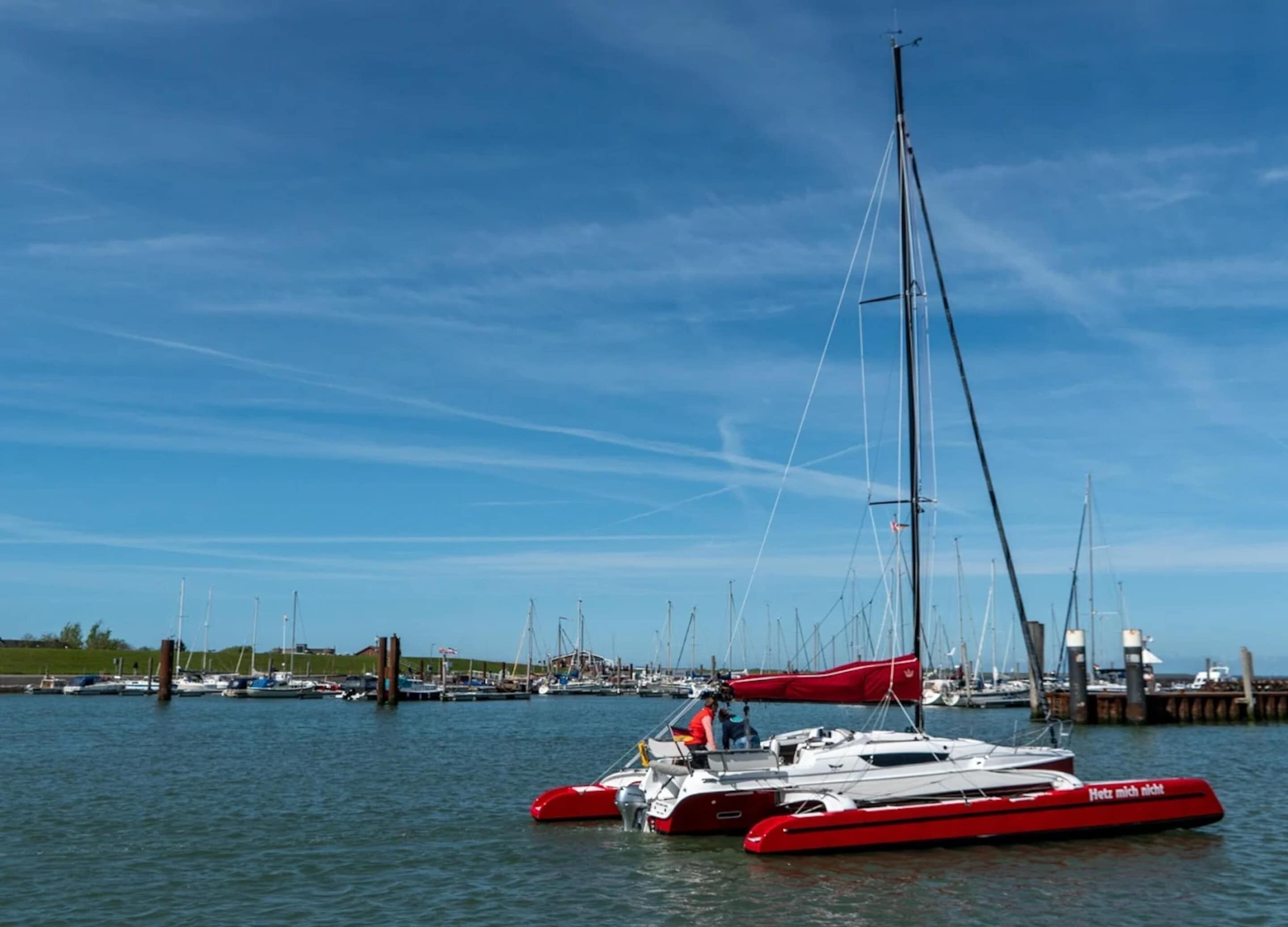 En småbåtshamn med flera segelbåtar förtöjda, bland annat en röd katamaran med en tysk inskription.