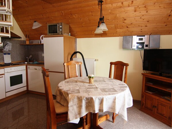 A compact kitchen with a dining area, including a table with a tablecloth, chairs, a microwave, a refrigerator, and a television. - Semi-detached Houses, Boltenhagen (Boltenhagen)