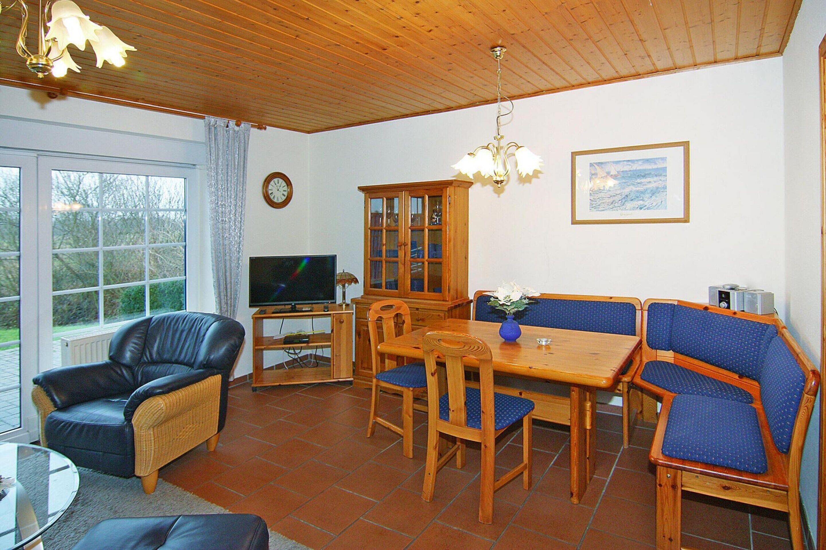 Ett möblerat vardagsrum med en tv, ett träskåp och ett matbord med blå klädda stolar.
