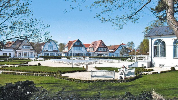 A row of traditional European-style houses with red roofs, a central open space with benches, and a white building with arched windows. - Semi-detached Houses, Boltenhagen (Boltenhagen)