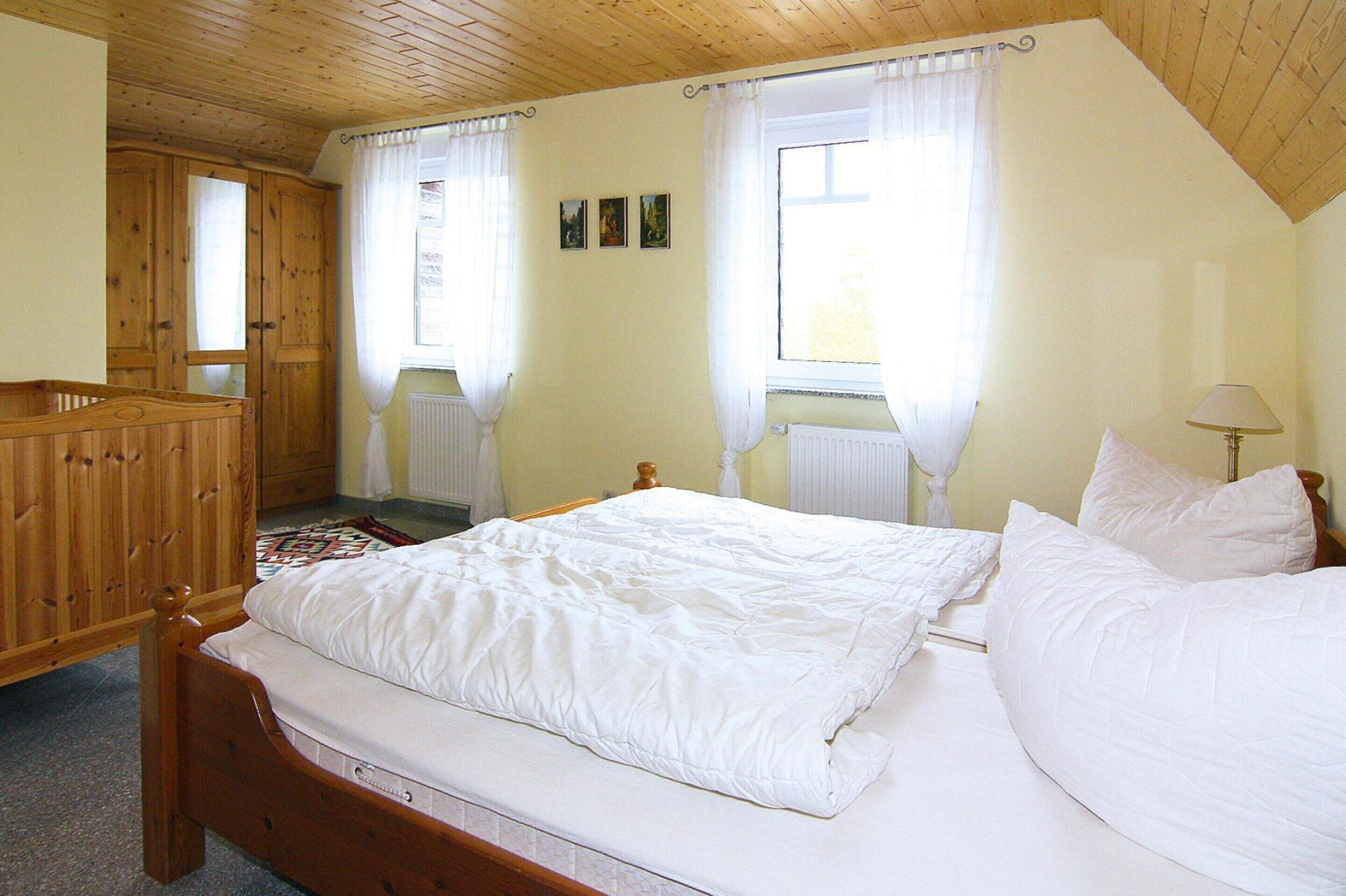 A bedroom with a wooden bed, a wooden wardrobe, and a window with curtains.