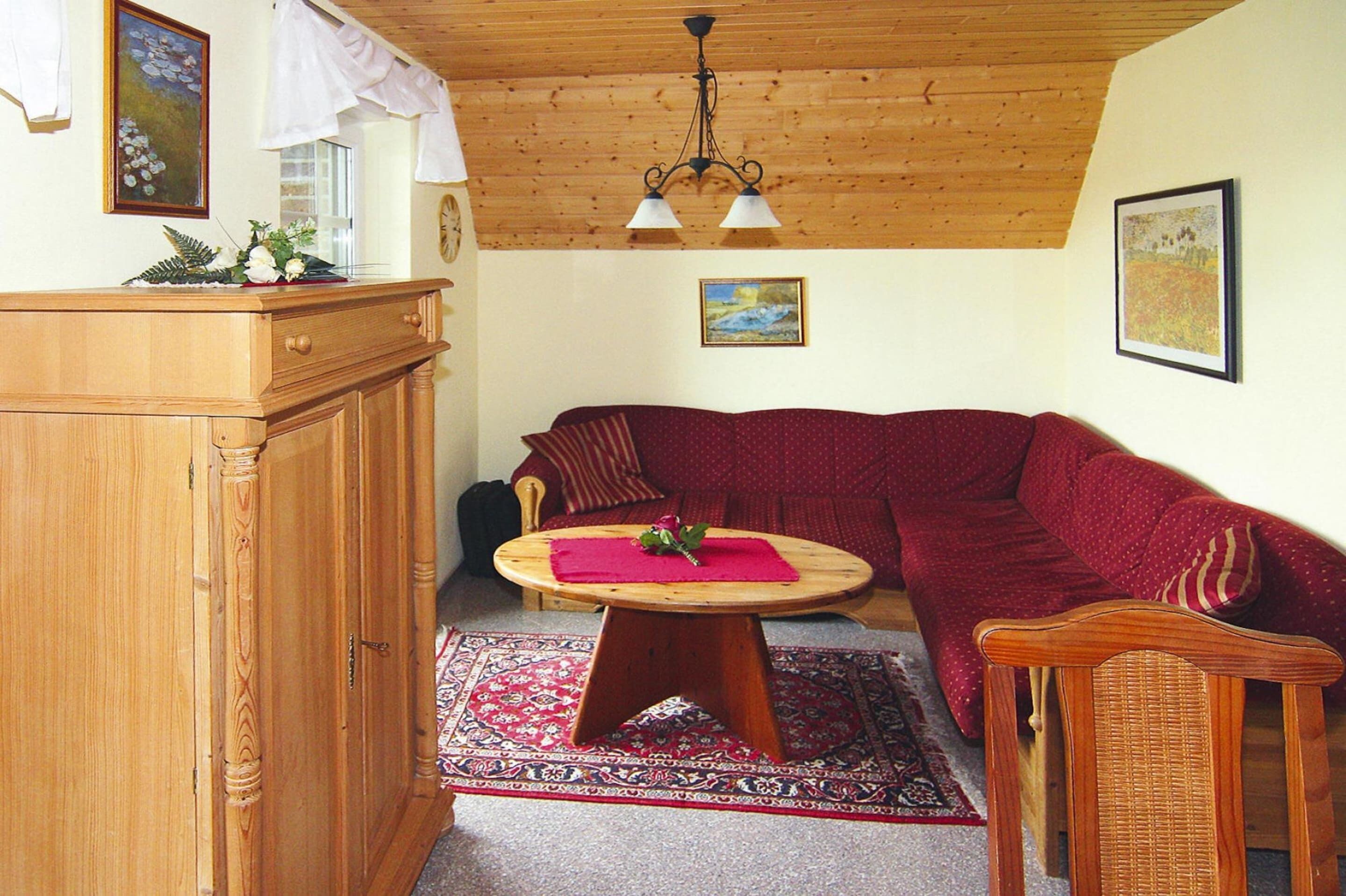 Una sala de estar acogedora con techo de madera, un sofá rojo, una mesa de madera con un mantel individual rojo y una alfombra estampada.