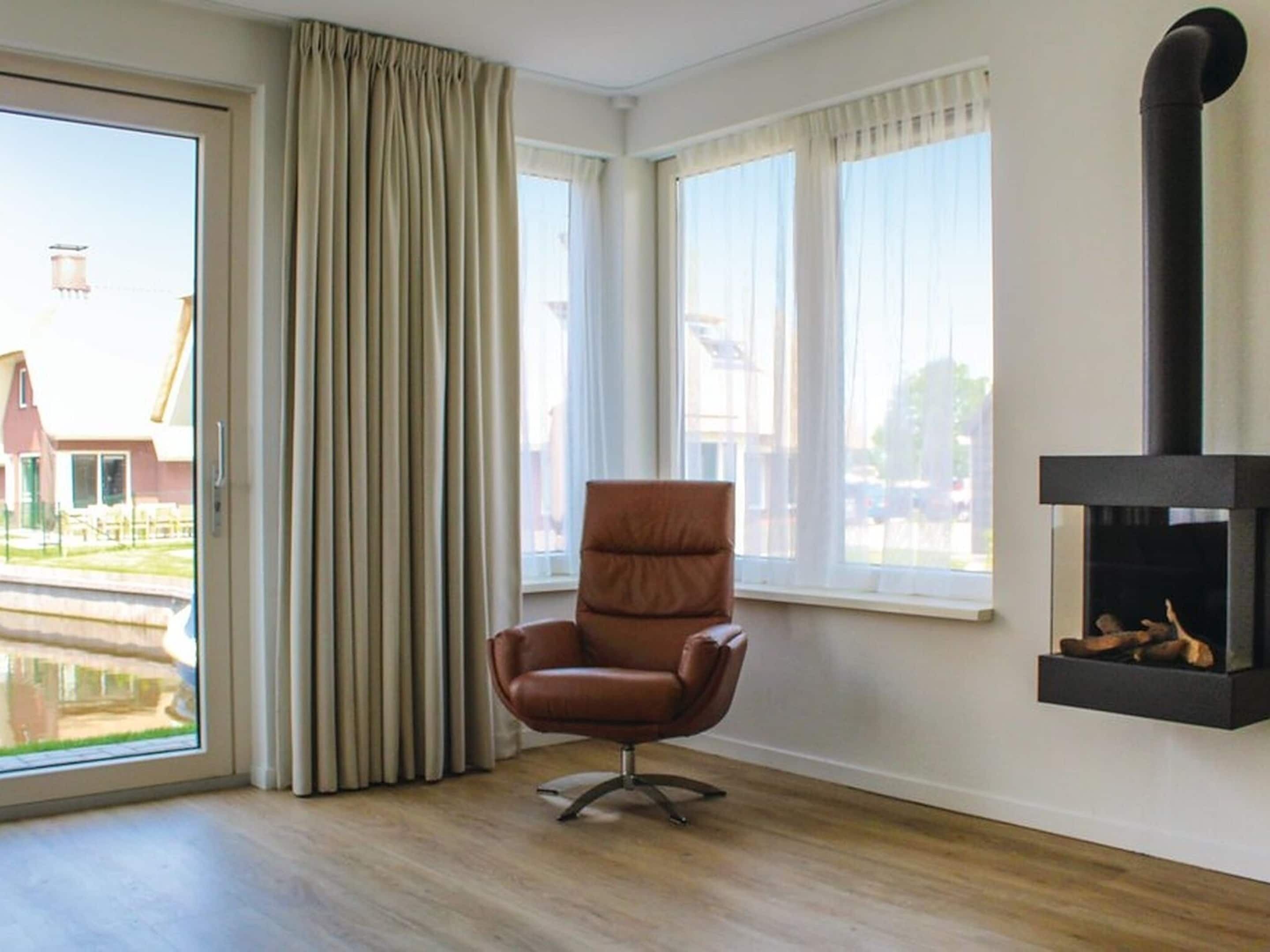 Ein Zimmer mit großem Fenster, einem braunen Ledersessel und einem schwarzen Kamin.