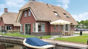 Una casa con techo de paja, un barco amarrado y un área de estar al aire libre.