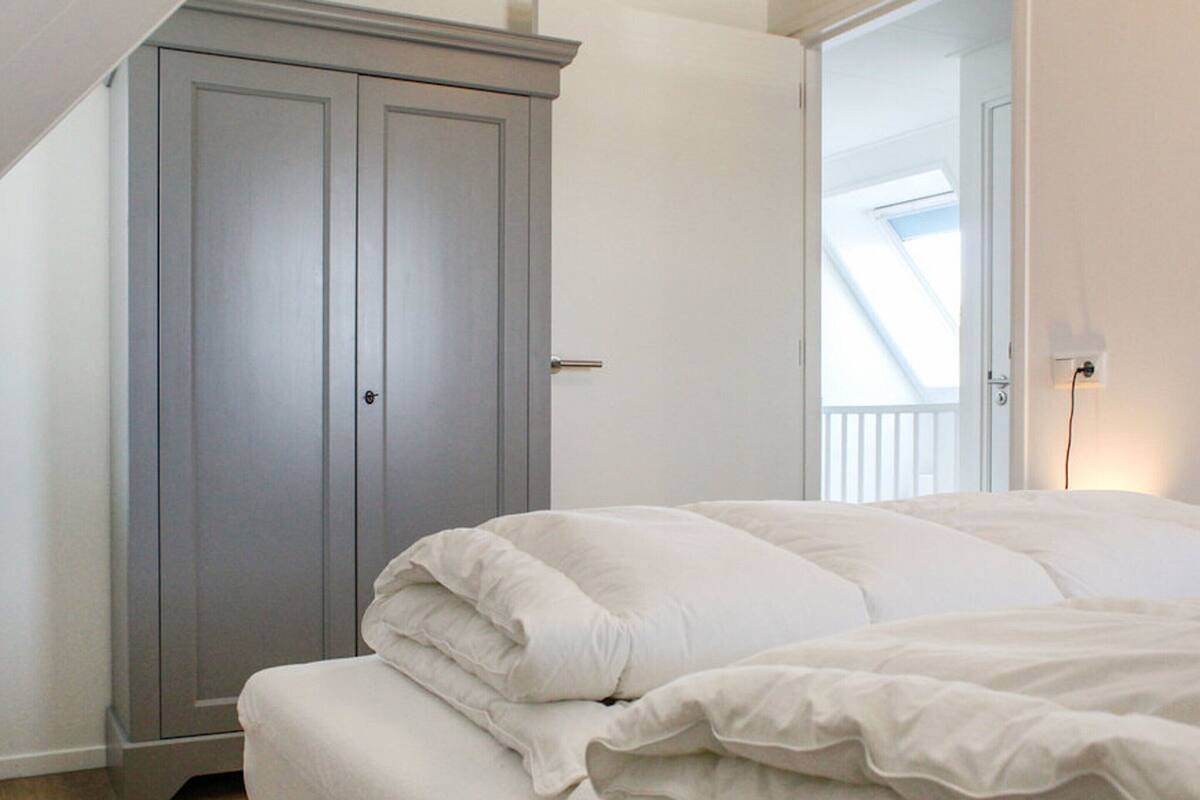Une chambre à coucher avec un lit, une armoire grise et une fenêtre donnant sur un beau paysage.