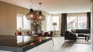Cocina moderna con una isla central, comedor con sillas y mesa, y sala de estar con sofá y lámpara.