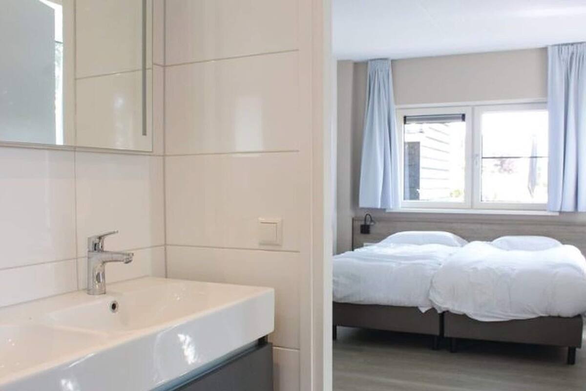 Une salle de bain moderne dotée d’un grand lavabo et d’un grand miroir, d’une douche séparée, et d’une chambre avec un lit et une fenêtre.