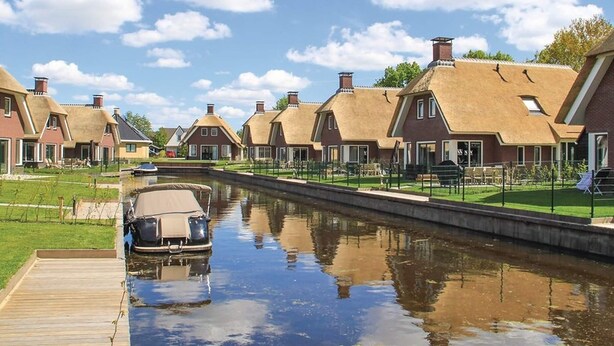 Una hilera de casas tradicionales con techos de paja, un canal y un muelle de madera.