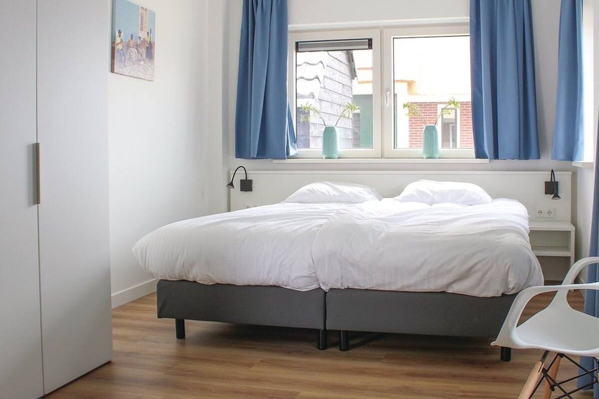 Une chambre à coucher avec un lit, une fenêtre avec des rideaux, une table de chevet et une chaise.