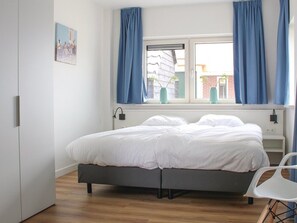 A bedroom with a bed, a window with curtains, a bedside table, and a chair.
