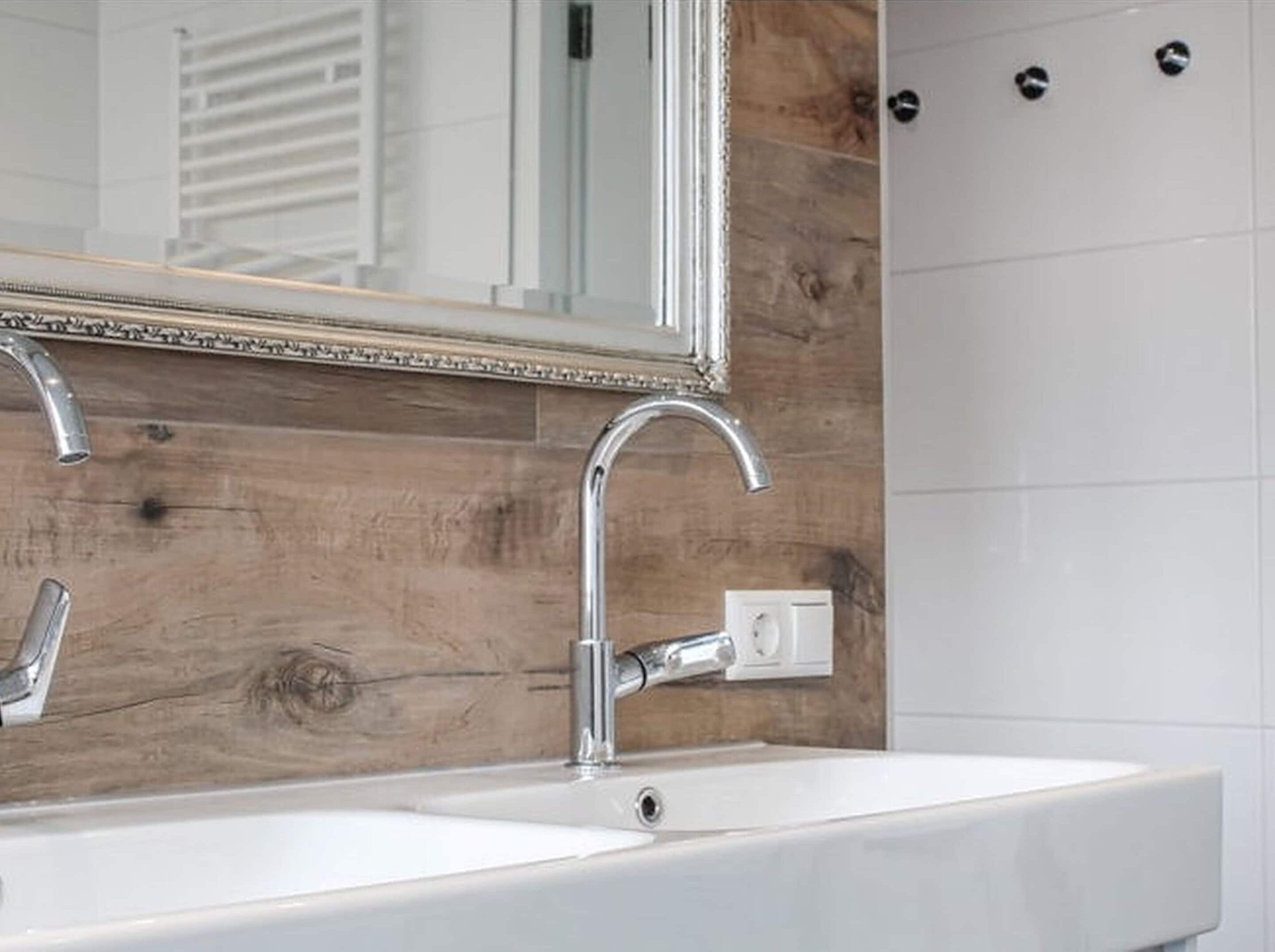 A bathroom with a wooden wall, a white sink, and a mirror with a decorative frame.