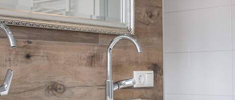 A bathroom with a wooden wall, a white sink, and a mirror with a decorative frame.