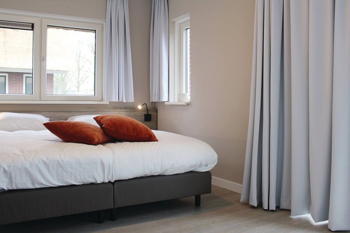 Une chambre à coucher avec un grand lit, deux fenêtres et des rideaux.