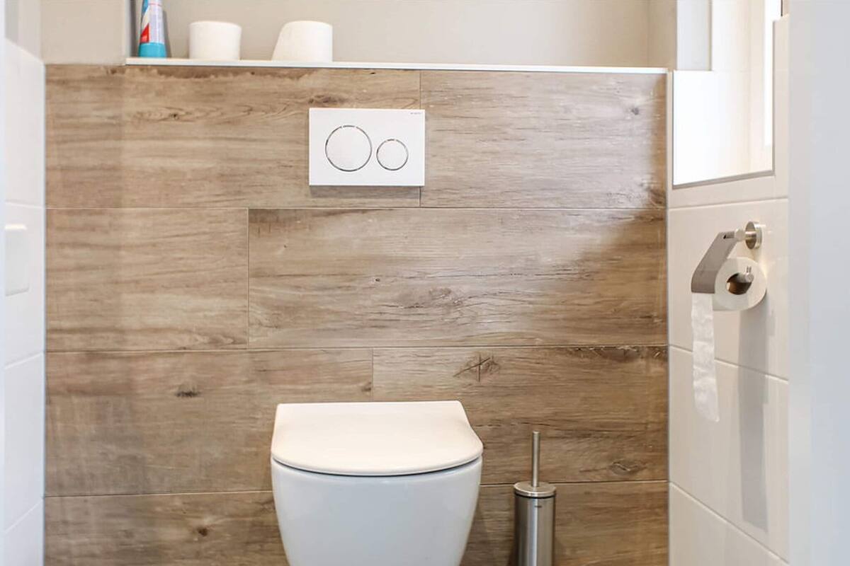 Une salle de bain moderne avec un mur en bois, des toilettes, un bidet et un porte-rouleau de papier toilette.