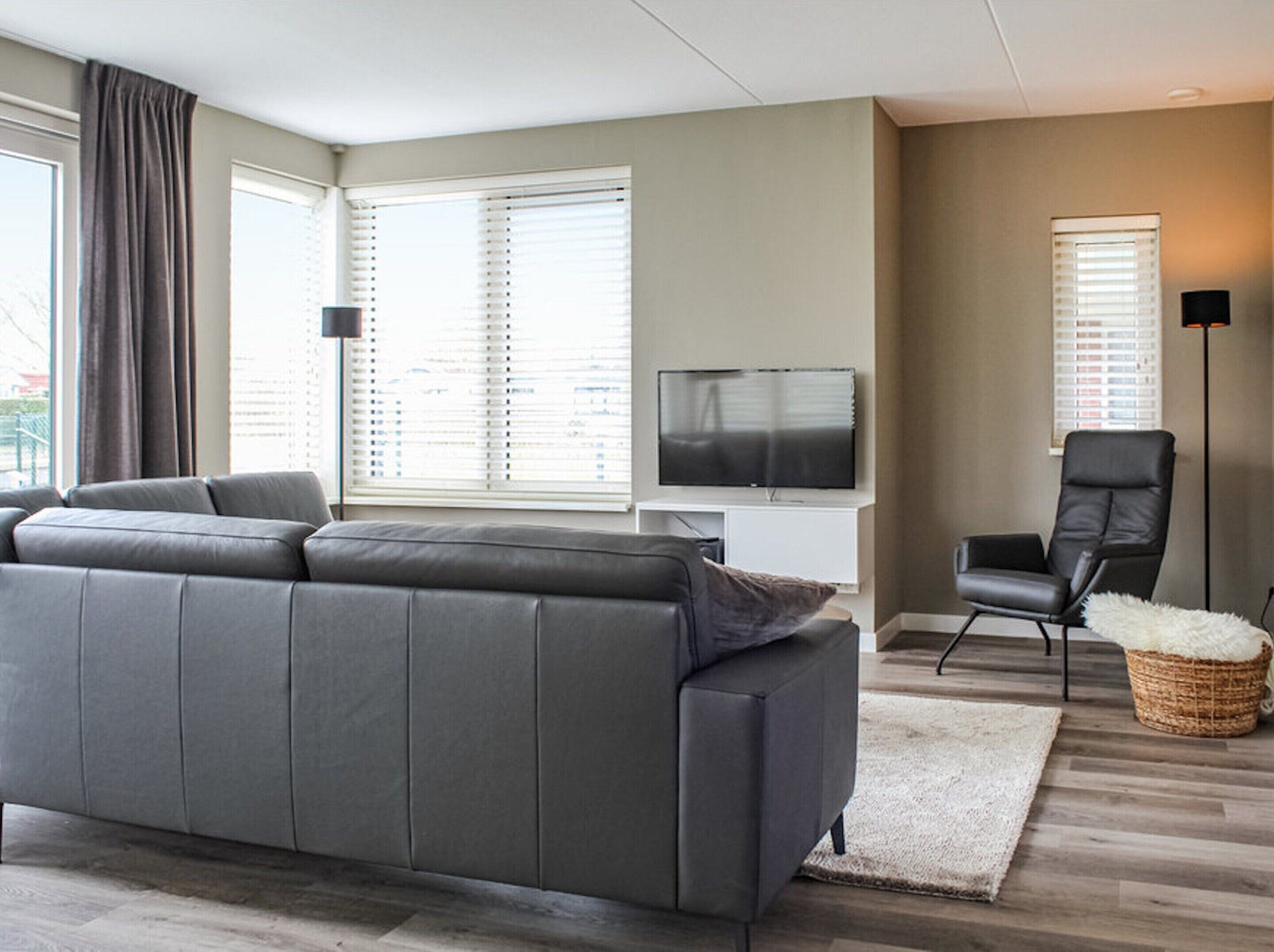 Un salon moderne avec un canapé gris, un téléviseur à écran plat, un fauteuil noir et une lampe sur pied.