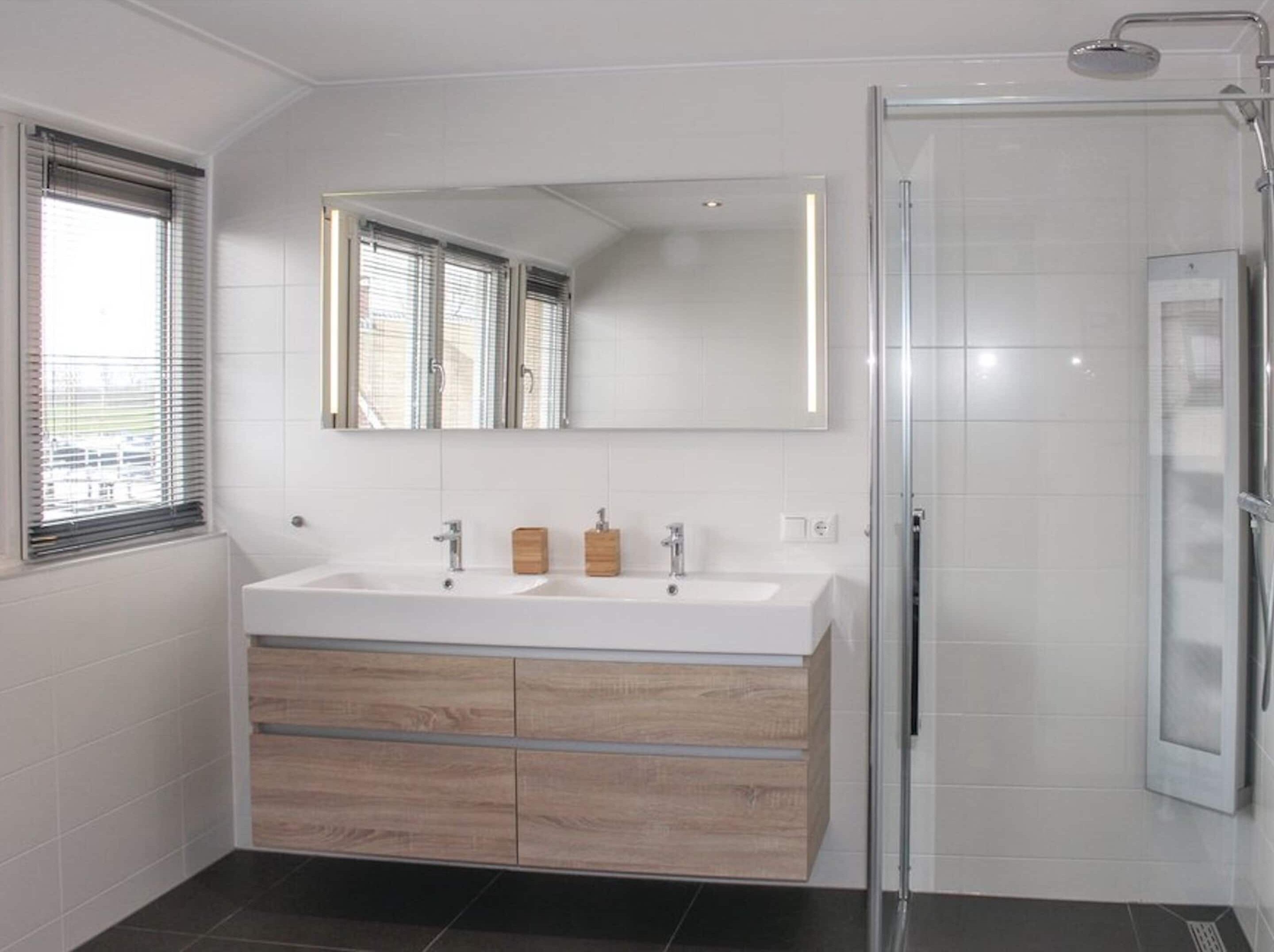 Een moderne badkamer met een wastafel met twee kommen, een grote spiegel en een douchecabine met glazen wanden.