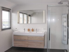 A modern bathroom with a double sink vanity, a large mirror, and a glass shower enclosure.