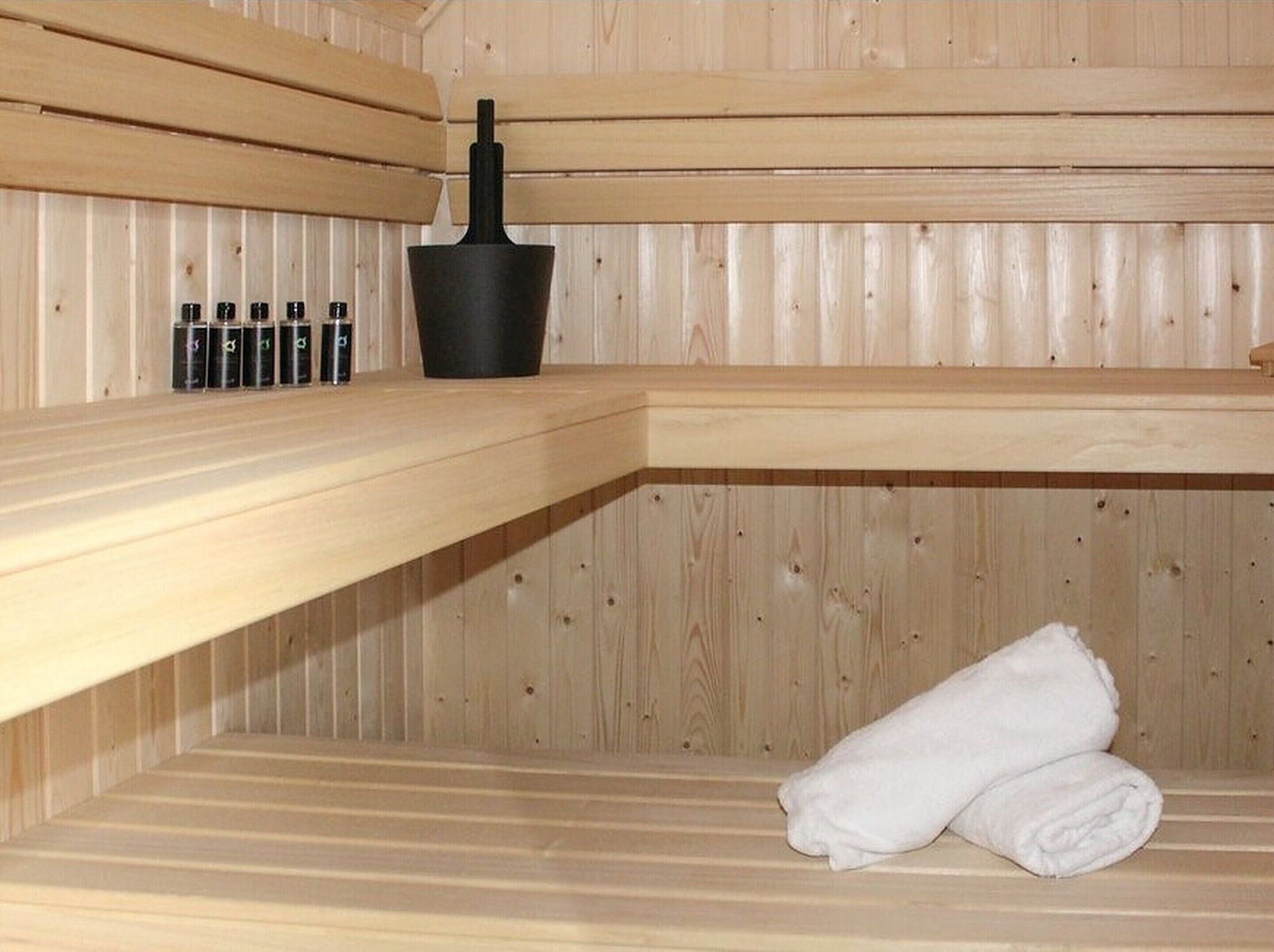 Een sauna met houten banken, een zwarte asbak en diverse olieflessen.